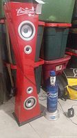 Full view of the tall red Budweiser branded Bluetooth tower speaker with four speaker drivers and silver rims, sitting on floor with storage bins behind it.