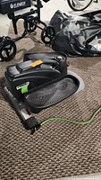 Full view of the Stamina inMotion E-3000 compact strider placed on carpet with visible foot pedals and part of the frame, along with a green resistance cord attached.