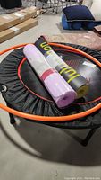 Photo shows Pelpo mini trampoline with orange trim, black mat, orange hula hoop on top and two rolled yoga mats (one purple Lululemon and a black WWWW)