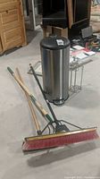 Wide shot showing trash can, brooms, and cultivator on floor indoors