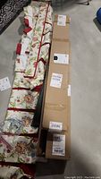 Four floral fabric valances on wood with brackets laid on floor beside two long cardboard boxes containing curtain rods.