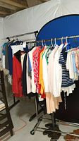 Full view of women's clothing on rolling rack, multiple tops, jackets, and sweaters visible in various colors and styles.
