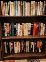 Three wooden shelves filled with novels in protective sleeves