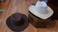 Photo showing both the brown leather and white wool felt cowboy hats together, highlighting materials and shapes.