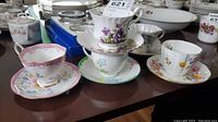 Five assorted porcelain cups with floral patterns and matching saucers arranged on a table.