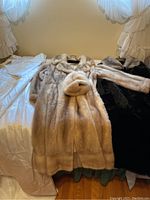 Photo shows two fur coats side by side on hangers, the lighter beige mink coat (Laskyss Emba) paired with a matching mink hat laid on top of the coat.