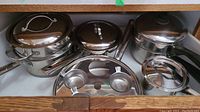 Wide shot showing Lagostina stainless steel pots with lids and a Coronet double boiler pot, along with a stainless steel kitchen item holder.