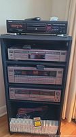 Full view of stereo stand with Teac CD recorder on top shelf, JVC components on middle shelves, and cassette tapes on bottom shelf along with speaker wire.