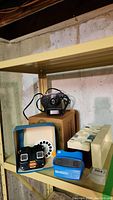 Shelf display showing boxed projector, black projector unit, two viewers, slide reel and slide boxes