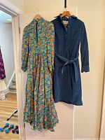 Two dresses hanging on wooden hangers, floral and navy blue dresses side by side