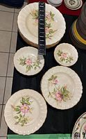 Overhead photo showing stacked plates and various sized floral patterned plates with measuring tape indicating approximately 10 inches diameter for large plates.
