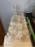 Eight clear glass drinking vessels on white surface showing front and sides with varied shapes and sizes including two pairs of wine glasses, martini glass, small stemmed glasses, and tall vase-like glass with staining near base.