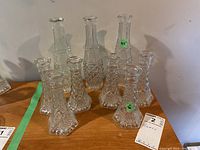 Photo showing nine glass vases: three taller 9.5-inch vases and six shorter 6-inch vases, arranged together on a wooden surface.