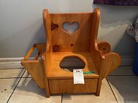 Wooden potty chair with heart-shaped cutout, side book holder, and toilet roll holder, viewed straight on and from above.
