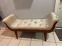 Front and side view of button-tufted upholstered bench showing cream fabric and wooden legs/frame, with visible stains and scratches on wood.