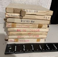 Stack of eight Super 8 film reels in their original cardboard sleeves, showing labels with dates and color/black & white indications alongside a ruler for scale.