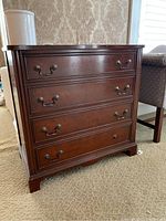Front view of a wooden chest with four drawers, two metal handles on each drawer except bottom drawer missing one handle. Surface has scratches and marks.