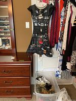 Black dress-shaped jewelry organizer hanging on wall with multiple clear pockets containing costume jewelry such as bracelets, earrings, and rings.
