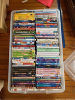 Top view of DVDs stacked inside a plastic tub, shows multiple kid-friendly titles including Toy Story 1-3, Elmo series, Moana, Frozen, and Princess themed DVDs.