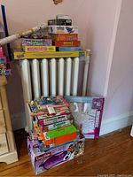 Stack of craft kits, board games, EasyBake oven box and painting kits stacked on a radiator beside a wall.