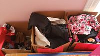 Three cardboard boxes showing a variety of girls clothing including snow pants, pajamas, and shoes.