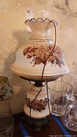 Full view of vintage hurricane lamp with painted flowers on top shade and base, metal base, and wrapped electrical cord.