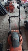 Front view of the Black and Decker LawnHog electric lawn mower showing the handlebar and mower housing on a concrete floor with some other items in the background.