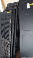Front view of stacked shutters, showing variety of louvered and solid panel shutters and attached metal hardware