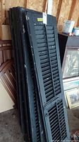 Stack of black wooden louvered shutters leaning against wall