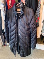 Black quilted long jacket hanging in closet view from front lengthwise