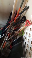 Photo of various yard tools including shovels with wooden and plastic handles, rakes, alongside the Lufkin measuring wheel handle visible.