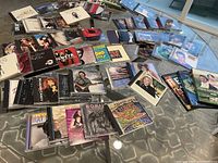 Photo shows a collection of approx. 60 music CDs laid out on a carpet with visible album covers including Bon Jovi, Ray Charles, and Lynyrd Skynyrd, along with 3 DVDs in cases.