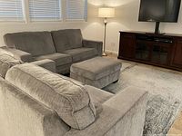 Light gray fabric couch with two seat cushions, two back cushions, and a matching ottoman, shown in a living room setting.