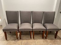 Front view of the four grey dining chairs lined up, showing upholstery and wooden legs.