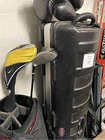 Close-up of golf clubs with covers, Nike golf bag, and hard travel case.