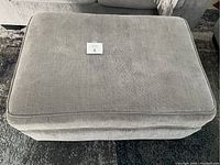 Top view of the light grey fabric ottoman showing cushioned surface and fabric texture