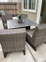 Four resin wicker chairs around square fire pit table on concrete patio
