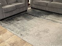 Photo showing main area of blue, grey, and beige textured area rug placed under couches on tiled floor.