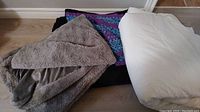 Set of blankets and duvet cover shown together on floor including white duvet, gray plush blanket, and colorful crochet blanket