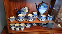 Blue and white Bombay style porcelain tea pot, coffee pot, tea cups with saucers, and cream and sugar containers displayed on upper shelf.