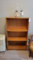 Front view of the wood bookcase with three shelves and two oil lamps placed on top. Shows size, color, and condition of bookcase.