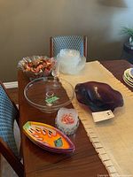Full view of lot on wooden table showing purple fruit bowl, clear pedestal cake plate, colorful boat-shaped dishes, salad bowl with potpourri, clear serving dishes, and wine glass.