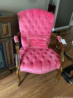 Full view of the rose-coloured armchair with tufted seat and back, wooden arms and legs, and matching pillow.
