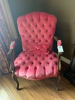 Front view of the armchair showing tufted pink upholstery, wood arms, and matching pillow.