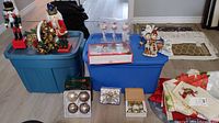 Wide shot showing a collection of Christmas decorations including nutcrackers, ornaments boxes, table linens, and storage bins