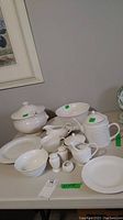 Photo of white ceramic dishware laid out on table showing bowls, platters, gravy boat, creamer, sugar bowl, salt and pepper shakers, plates, cups, and tureen.