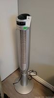Full view of the 46 inch tall silver WindChaser tower fan standing on the floor with power cord visible.