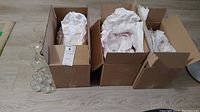 Three open cardboard boxes filled with assorted glassware wrapped in paper for protection