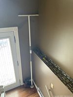 Full view of the white adjustable medical assist pole installed floor to ceiling in corner near door and wall.