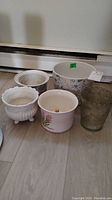 All five planters grouped together on a floor, showing variety of materials and designs with visible soil residue.
